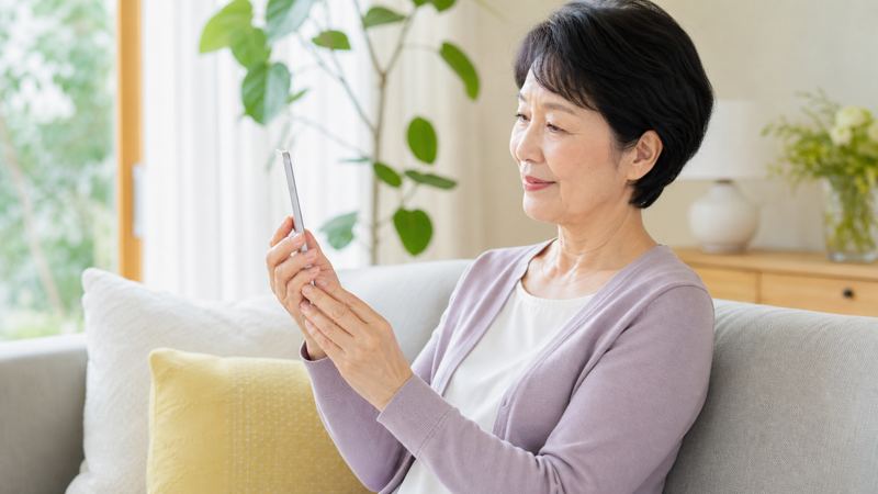 ソファで落ち着いてスマホを見ているシニア女性